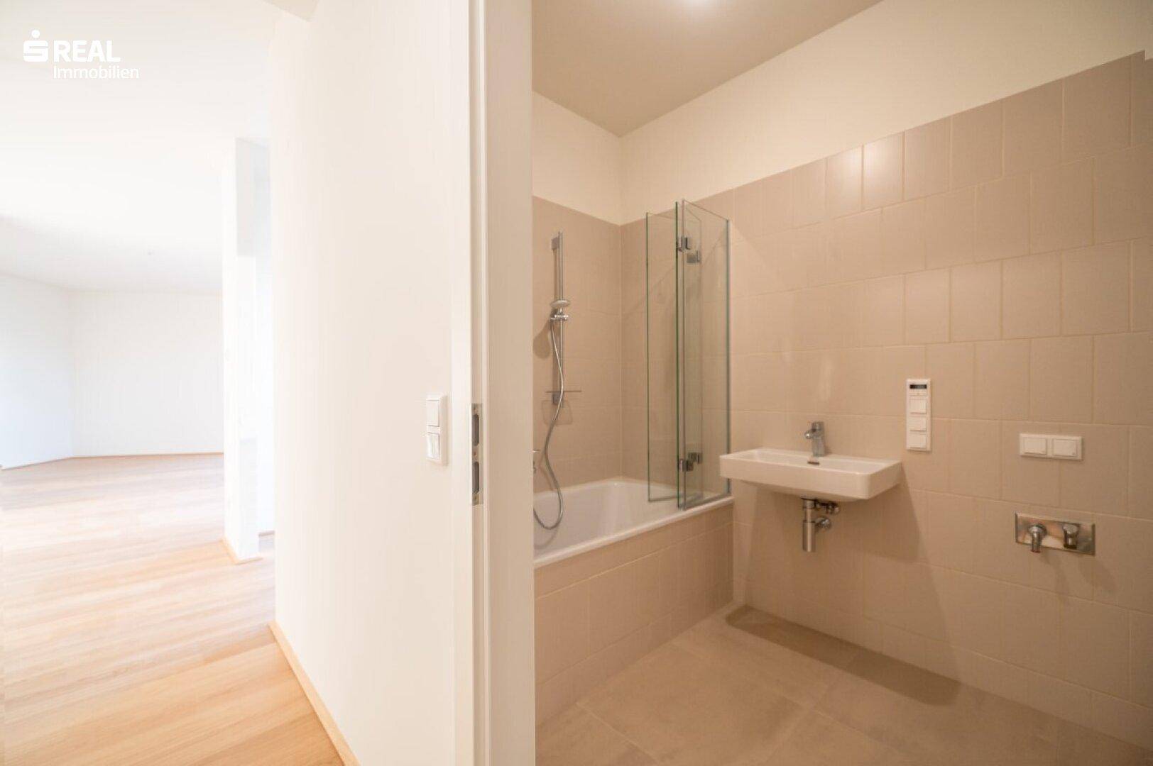 Helles Badezimmer mit Badewanne, modernem Waschbecken und beigefarbenen Fliesen.