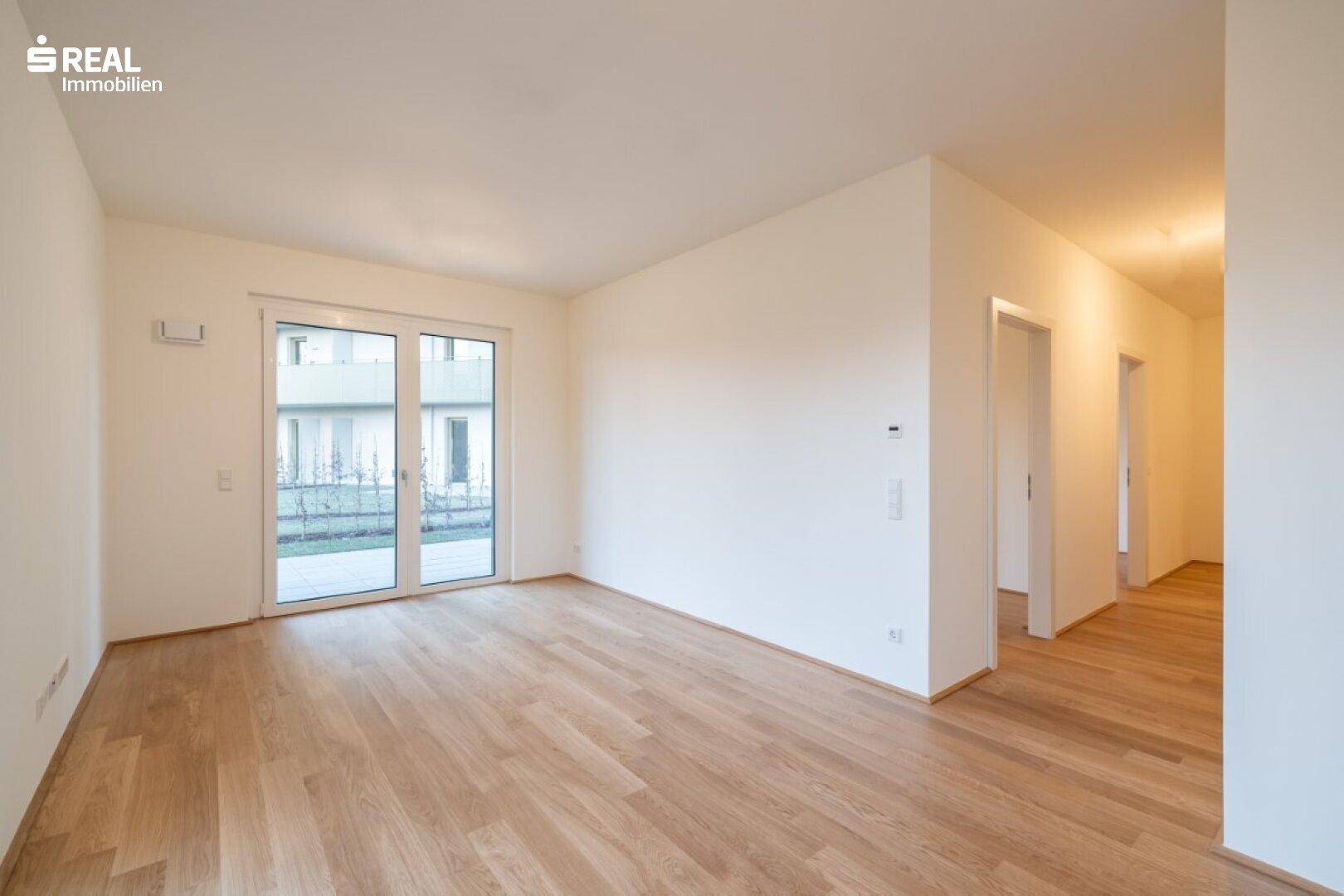Heller, leerer Wohnraum mit Holzboden und großem Schiebetürzugang zu einer Terrasse.
