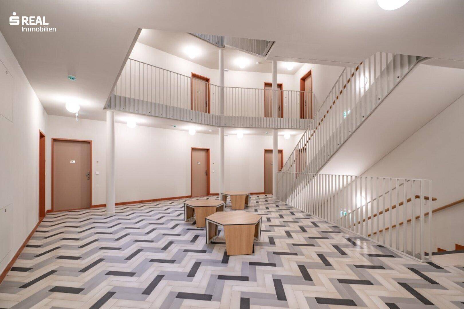 Geräumiger, heller Treppenhausbereich mit Sitzgelegenheiten und modernem Design.
