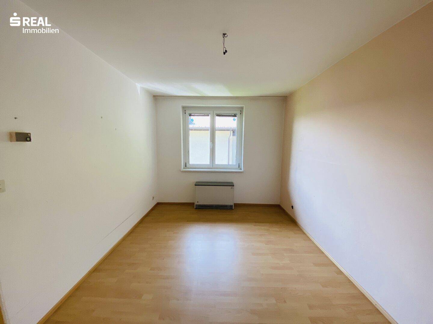 Helles Schlafzimmer mit Laminatboden und einem Fenster, das viel Tageslicht hereinlässt.
