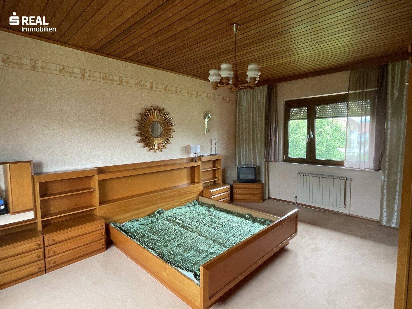 Schlafzimmer mit Holzbett, Holzdecke und Blick auf die Umgebung durch das Fenster.