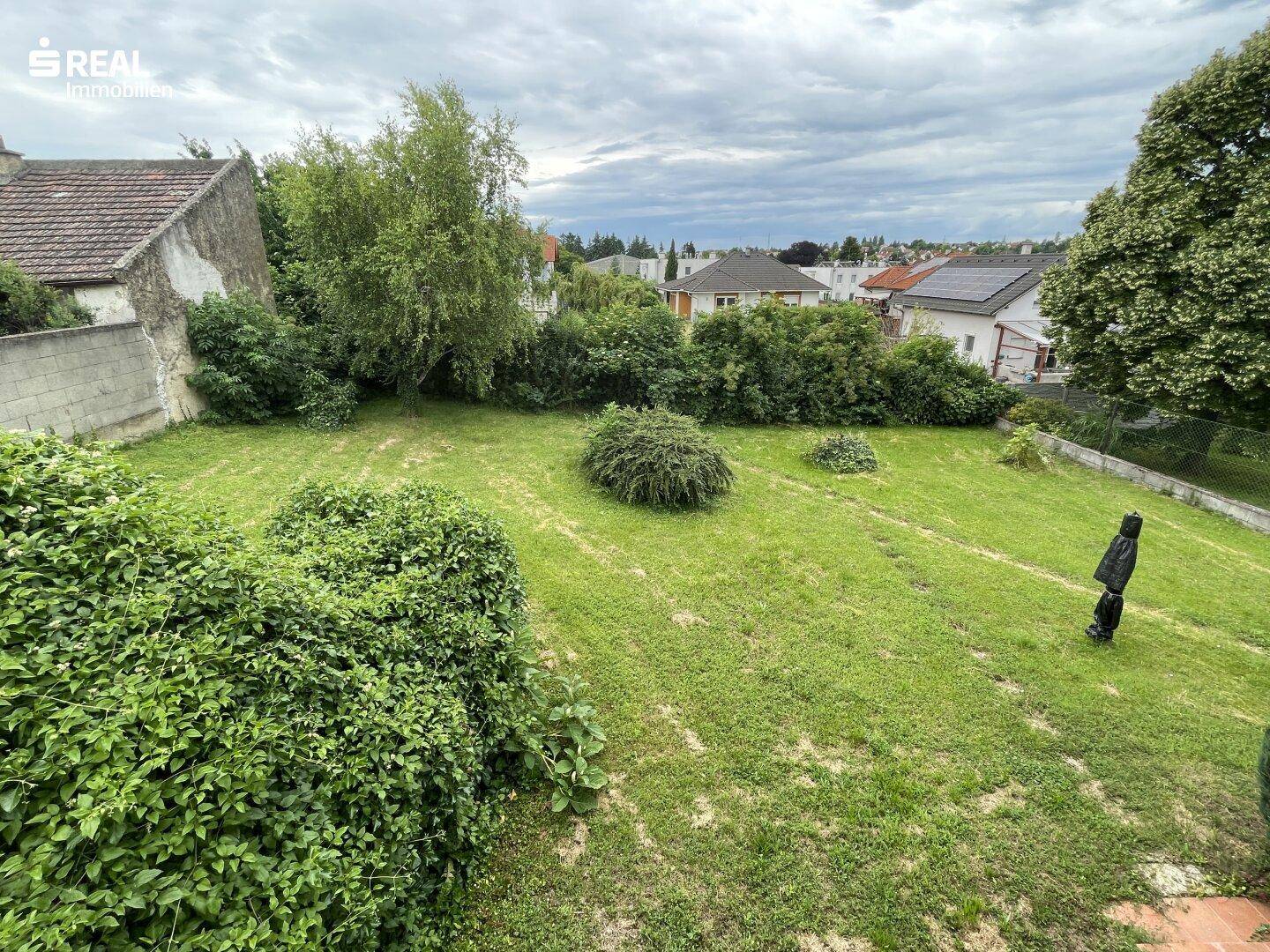 Großer, gepflegter Garten mit Rasenfläche und üppiger Bepflanzung, umgeben von Wohnhäusern.