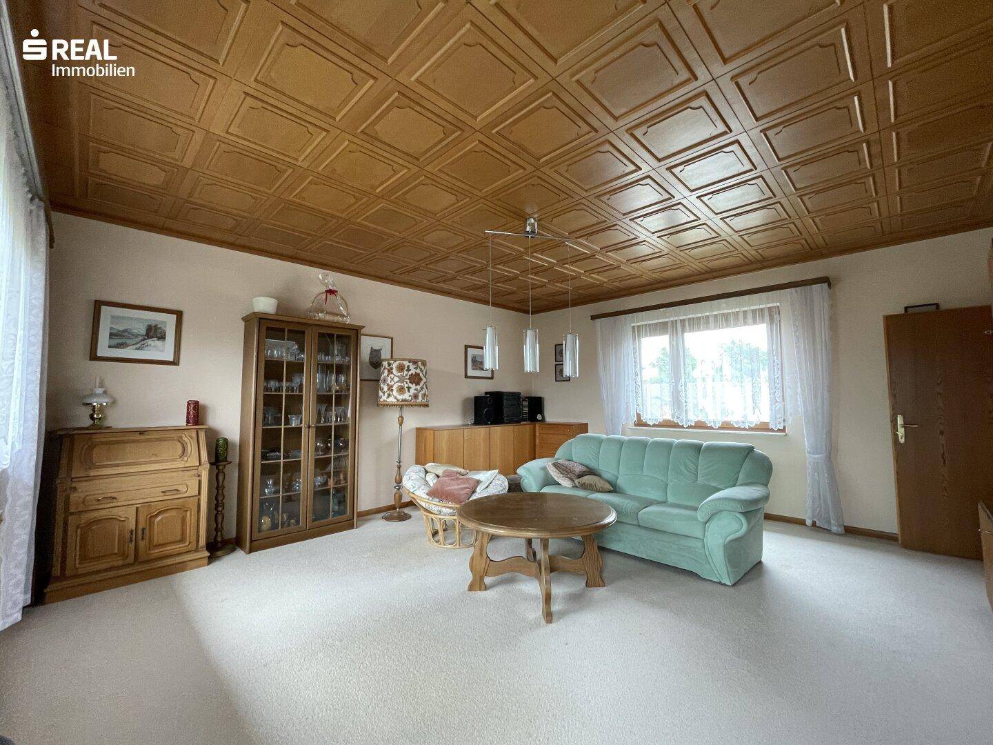 Geräumiges Wohnzimmer mit Holzdecke, Teppichboden und bequemen Sitzmöbeln.