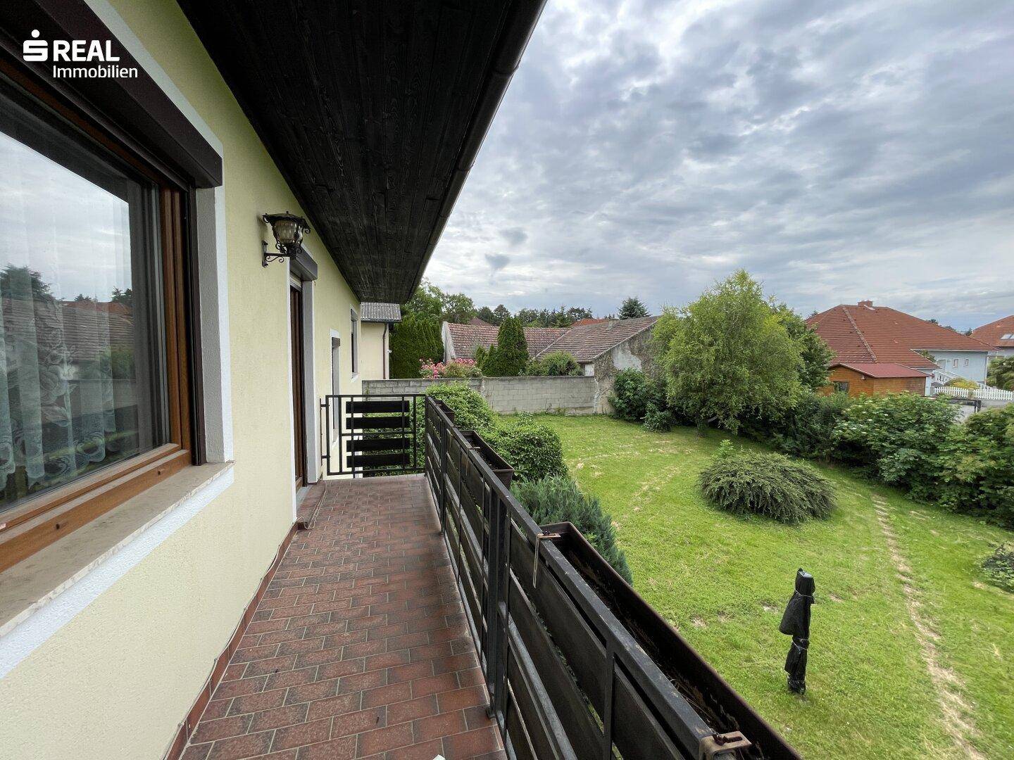 Geräumiger Balkon mit Ziegelboden und Blick auf den grünen Garten und die umliegende Nachbarschaft.