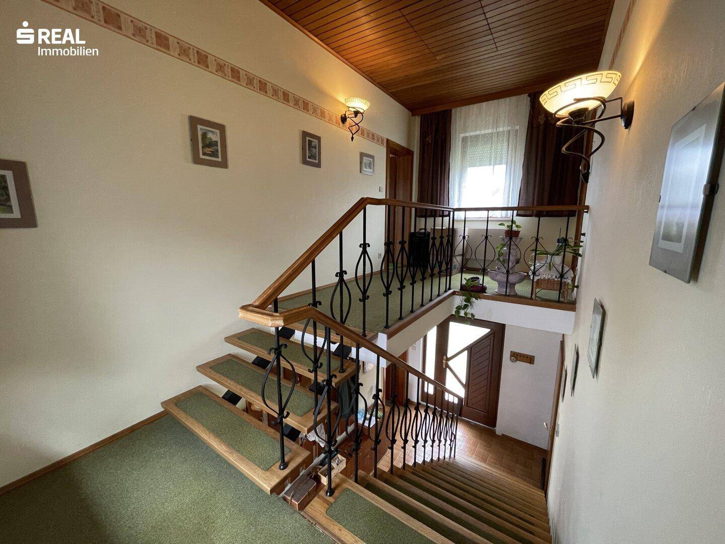 Treppenhaus mit Holzstufen und schmiedeeisernem Geländer, das die Etagen verbindet.