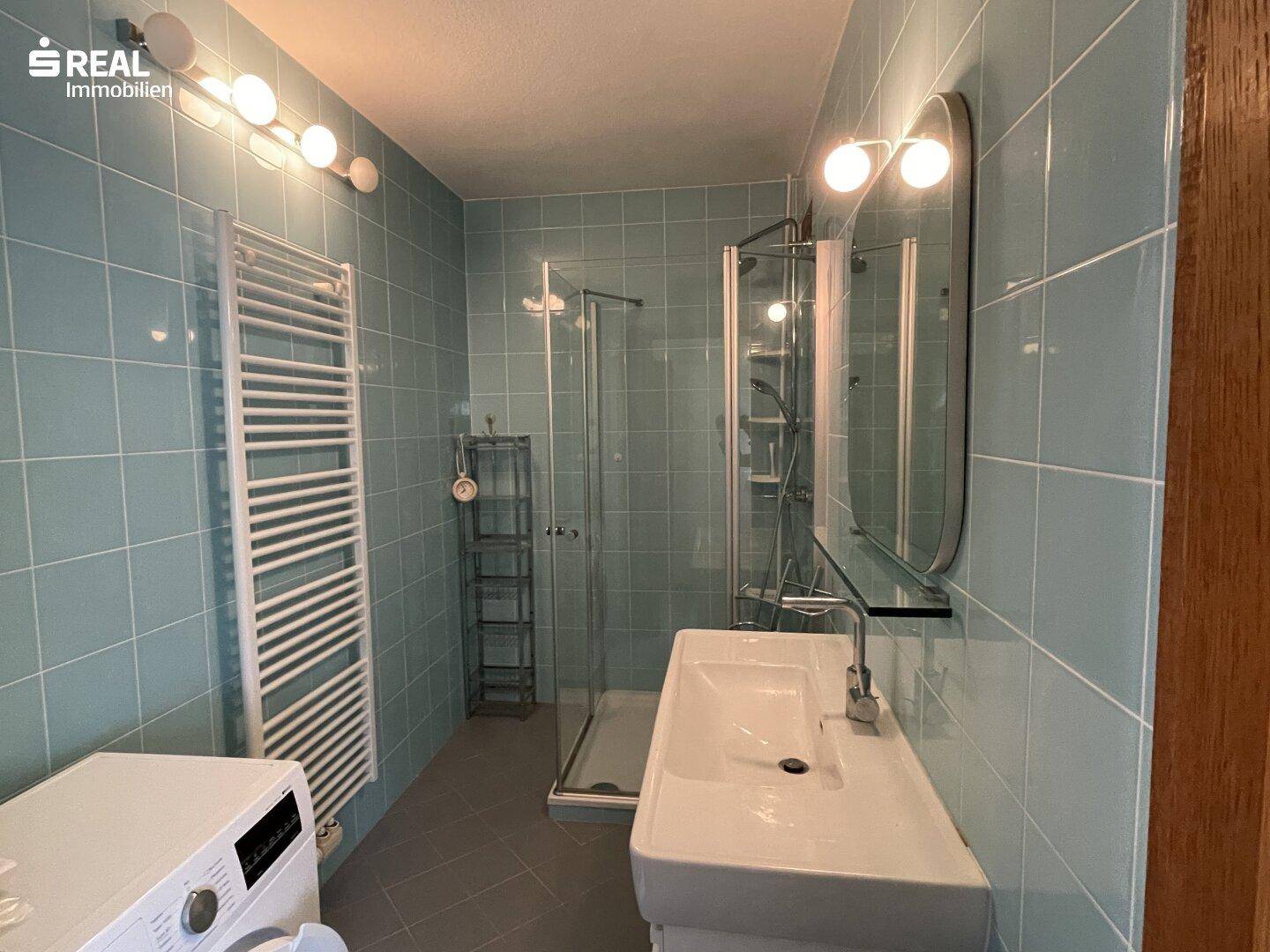 Modernisiertes Badezimmer mit hellblauen Fliesen, Dusche und beheiztem Handtuchhalter.