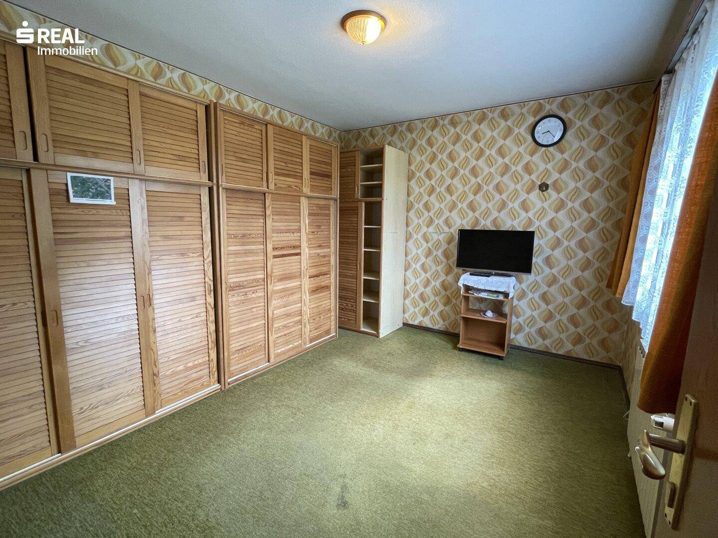 Schlafzimmer mit großen Einbauschränken, Teppichboden und gemusterter Tapete.