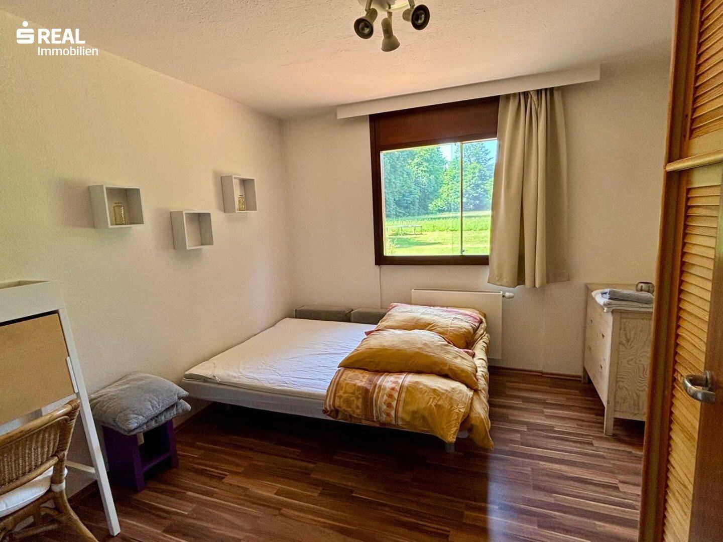 Schlafzimmer mit Einzelbett, Holzboden und Fenster mit Blick ins Grüne.