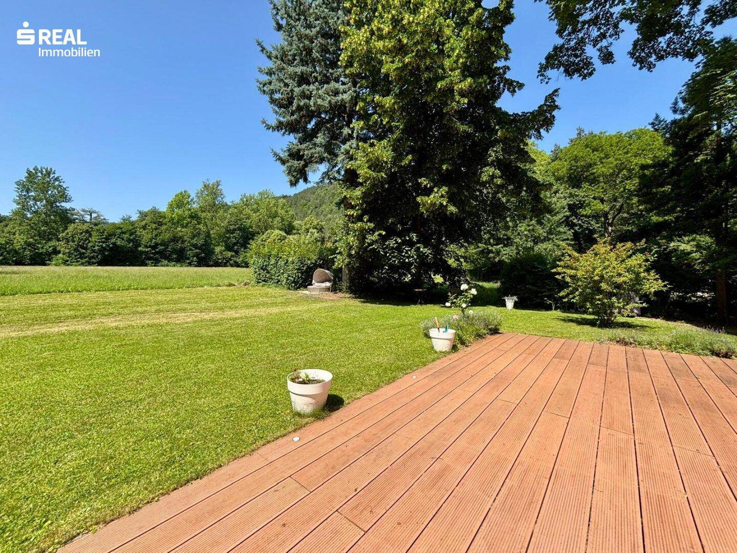 Holzterrasse mit Blick auf die weite Rasenfläche und die umliegende Natur.