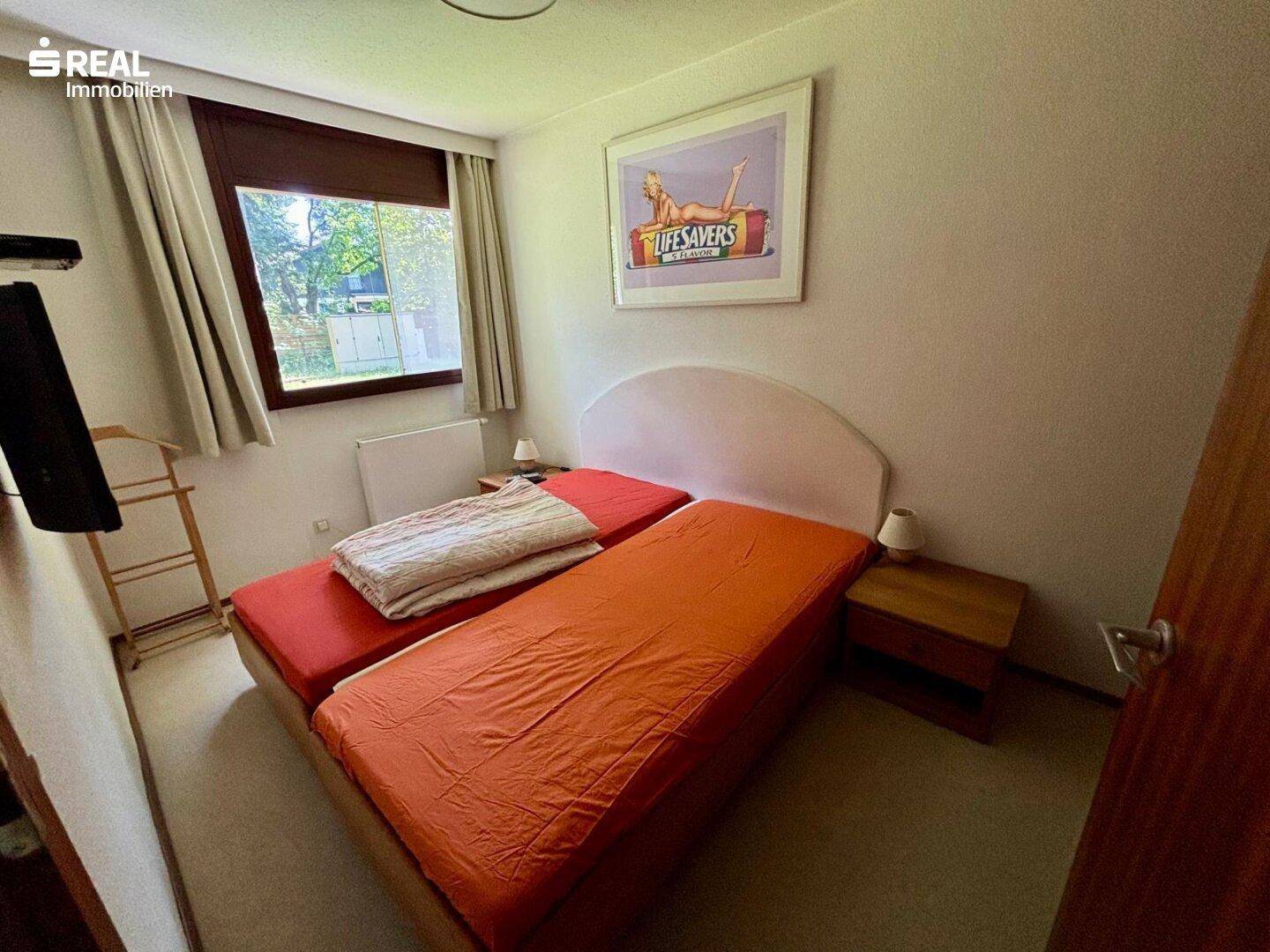 Helles Schlafzimmer mit zwei Einzelbetten, Holzboden und Blick ins Grüne.
