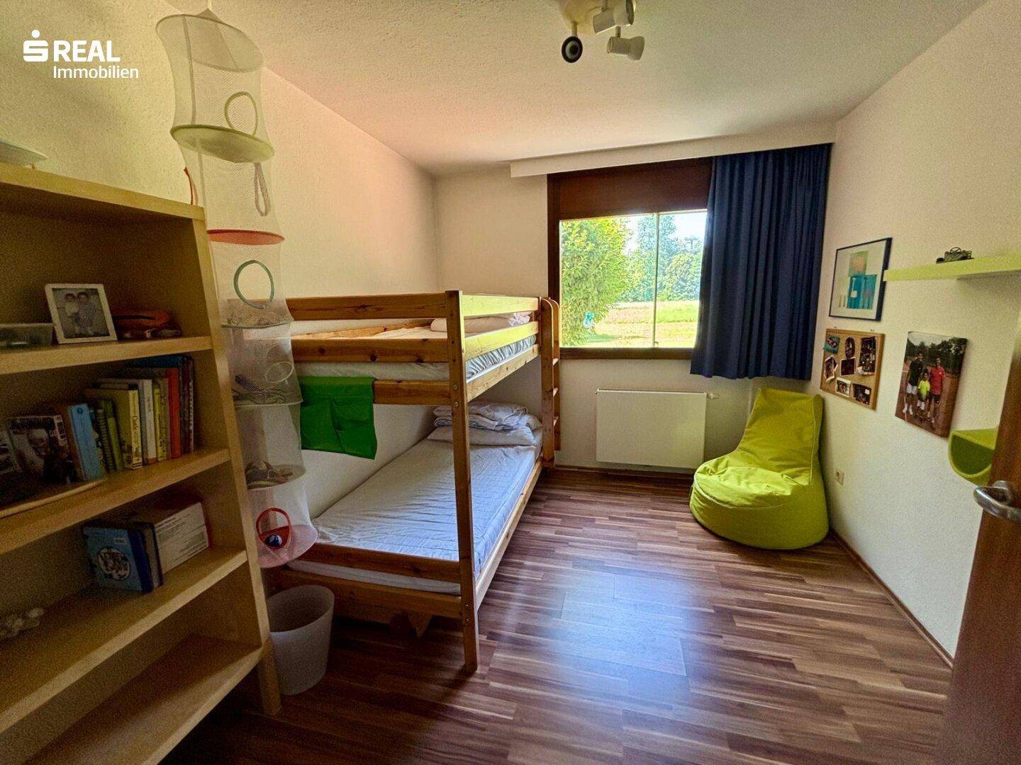 Kinderzimmer mit Etagenbett, Holzboden und Fenster mit Blick auf die Natur.
