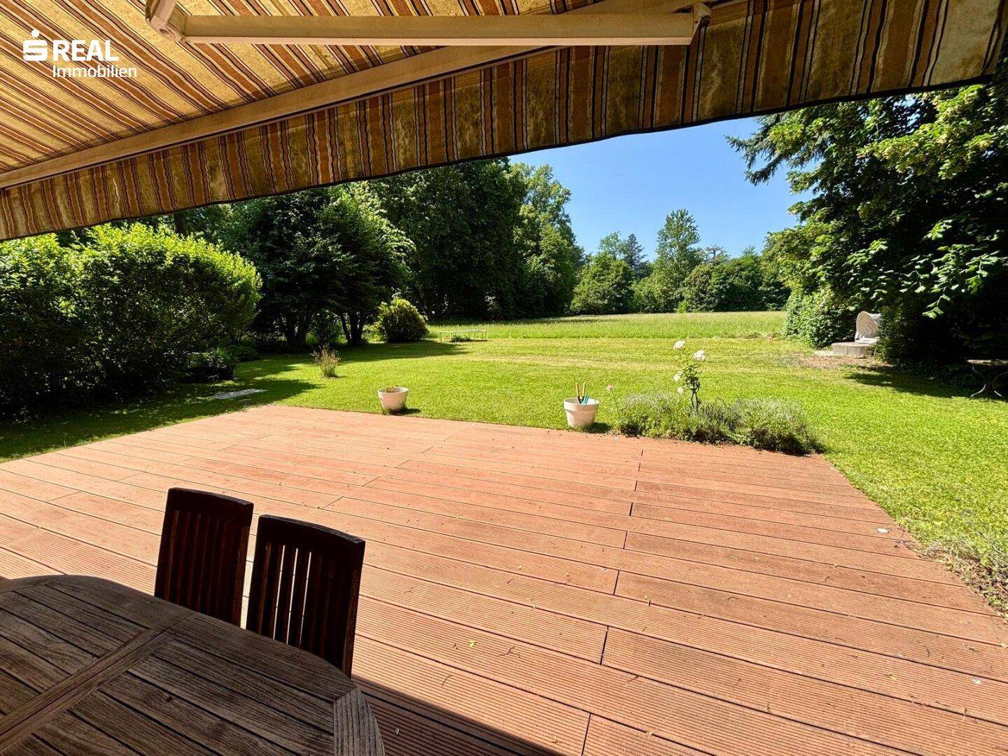 Überdachte Terrasse mit Esstisch und weitem Blick über den grünen Garten.
