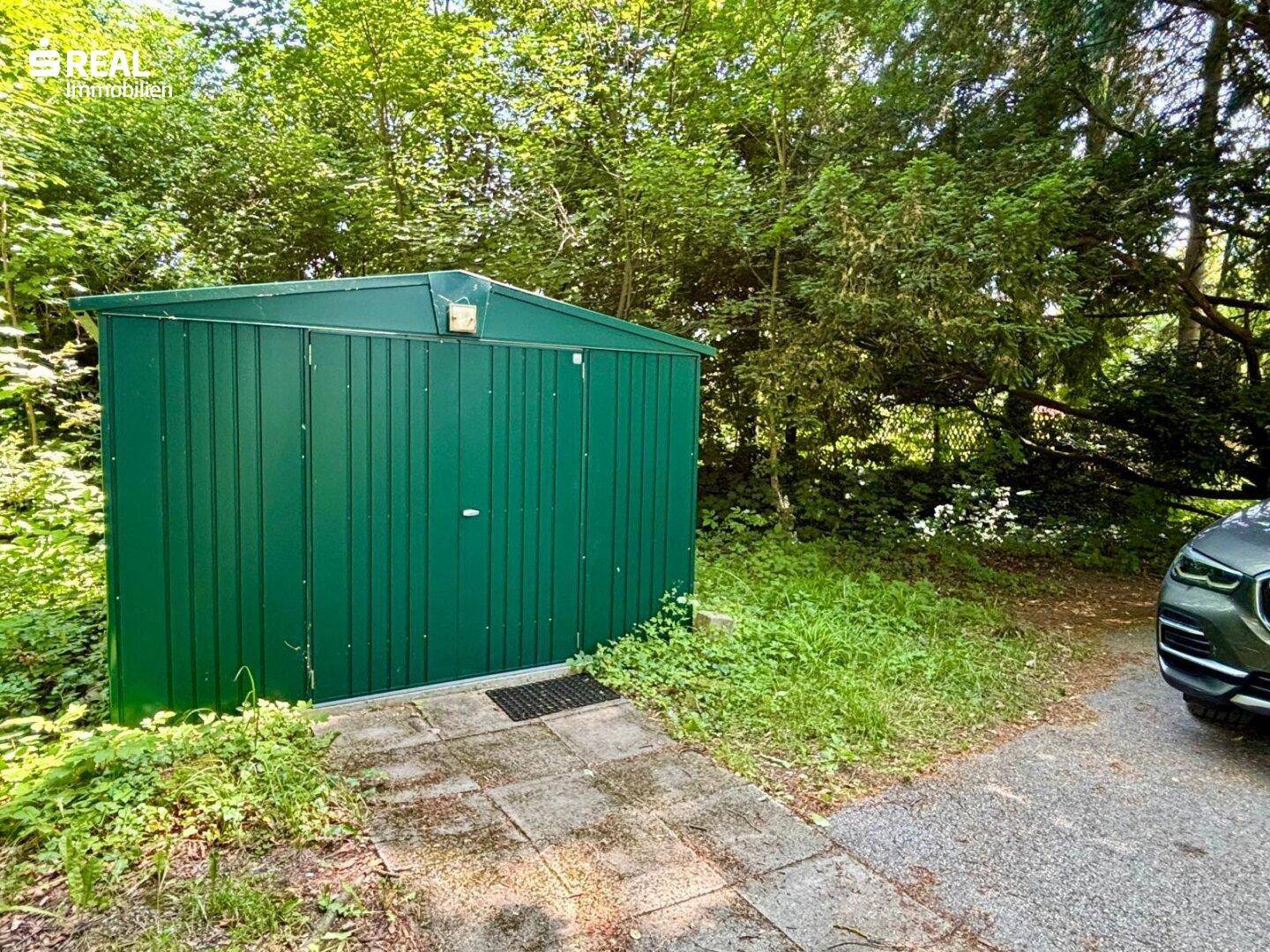 Grüner Gartenschuppen für Werkzeuge und Lagerung, umgeben von Bäumen.