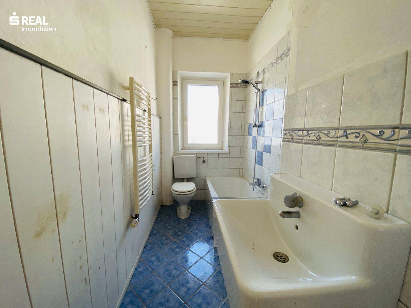 Badezimmer mit blauen Fliesen, Badewanne, Waschbecken, WC und Handtuchheizkörper.