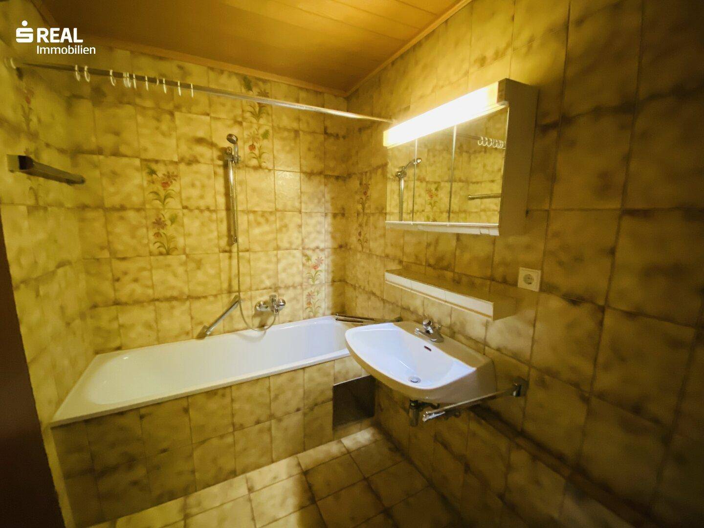 Badezimmer im Stil der 80er Jahre mit Badewanne, Waschbecken und gemusterten Fliesen.