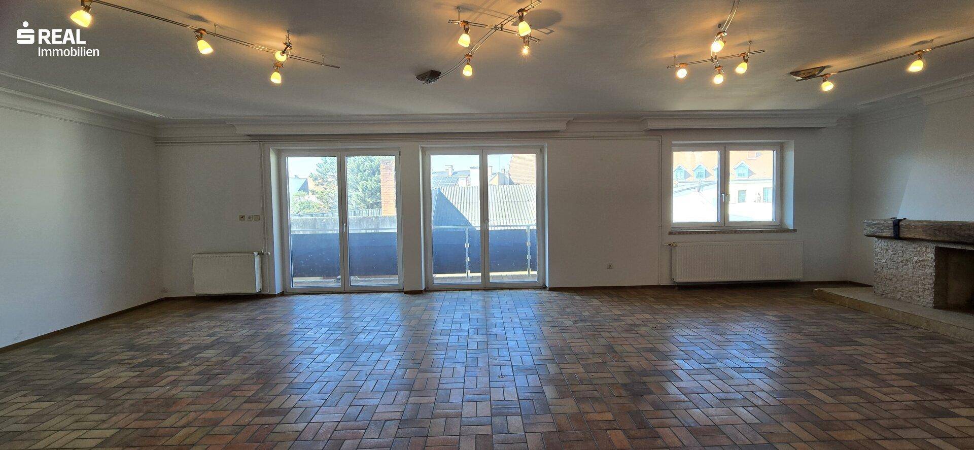 Großes Wohnzimmer mit Parkettboden, vielen Fenstern und einem gemauerten Kamin an der Wand.