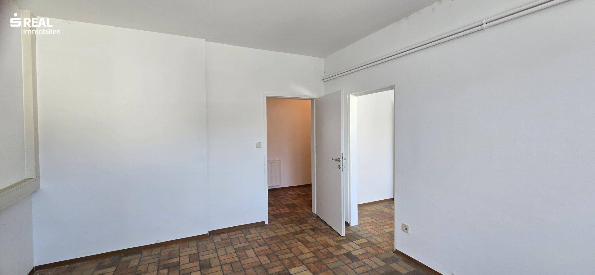 Leeres Zimmer mit Parkettboden und zwei offenen Türen, die zu weiteren Räumen führen.