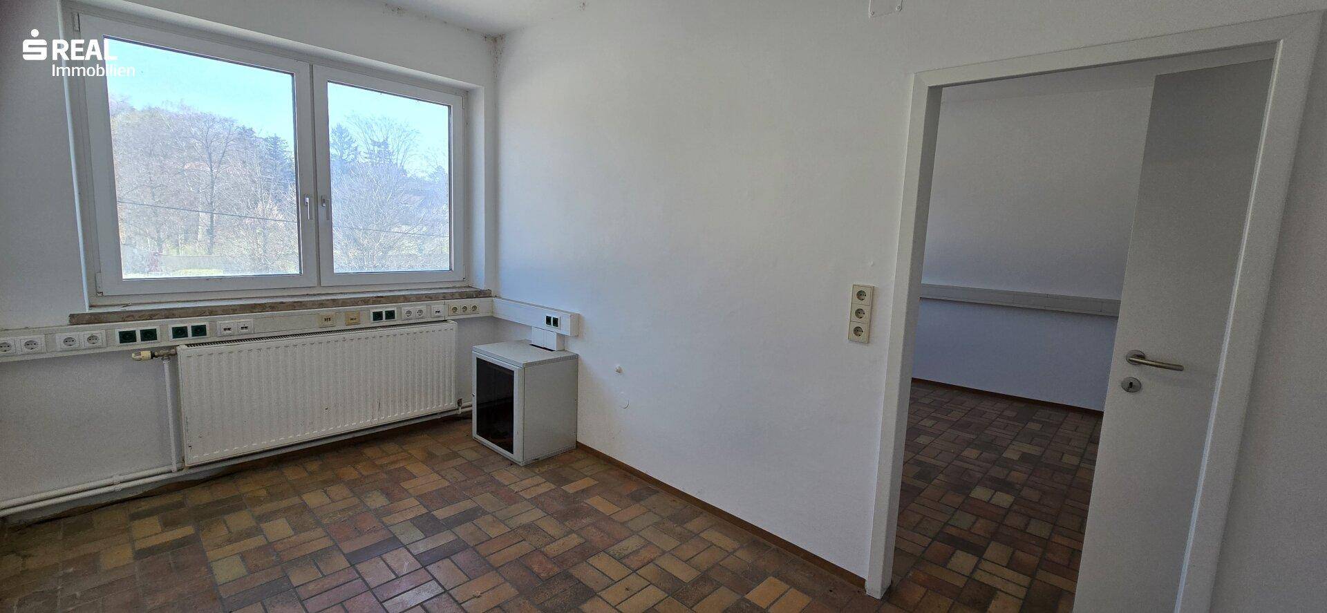 Helles Zimmer mit Parkettboden und einem Fenster, das einen Blick auf die Umgebung ermöglicht.