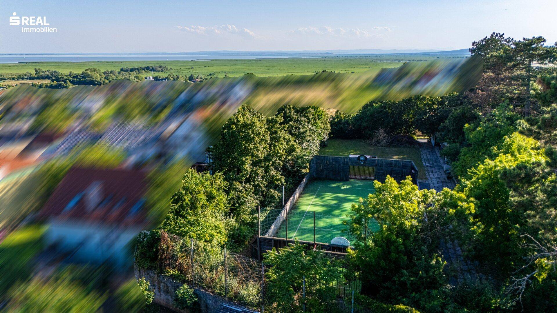 Panoramablick auf den Tennisplatz und die umliegende Wohnsiedlung mit weitem Blick auf den See.