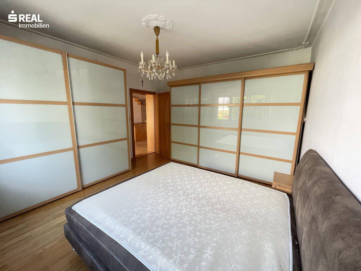 Schlafzimmer mit Parkettboden, großem Schiebetürenschrank und klassischem Kronleuchter.