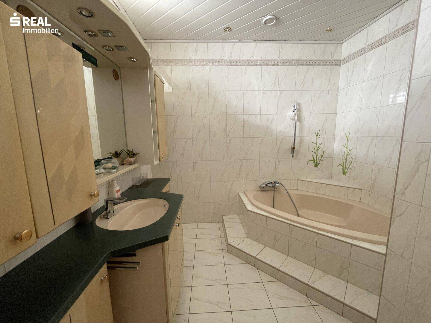 Badezimmer mit beigefarbenen Fliesen, Eckbadewanne und Waschtisch mit Spiegelschrank.