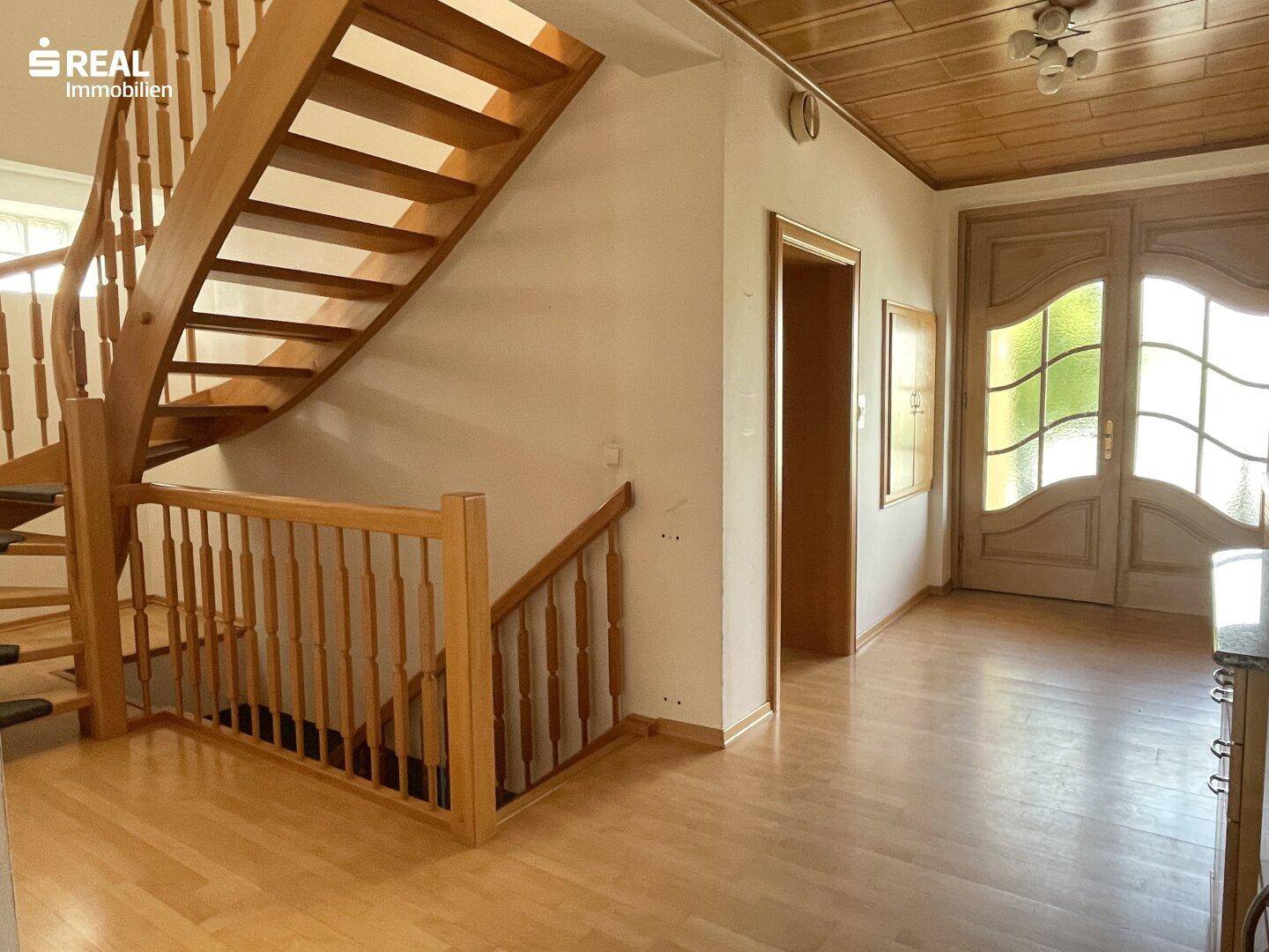 Heller Eingangsbereich mit Holztreppe, Parkettboden und einer dekorativen Haustür.