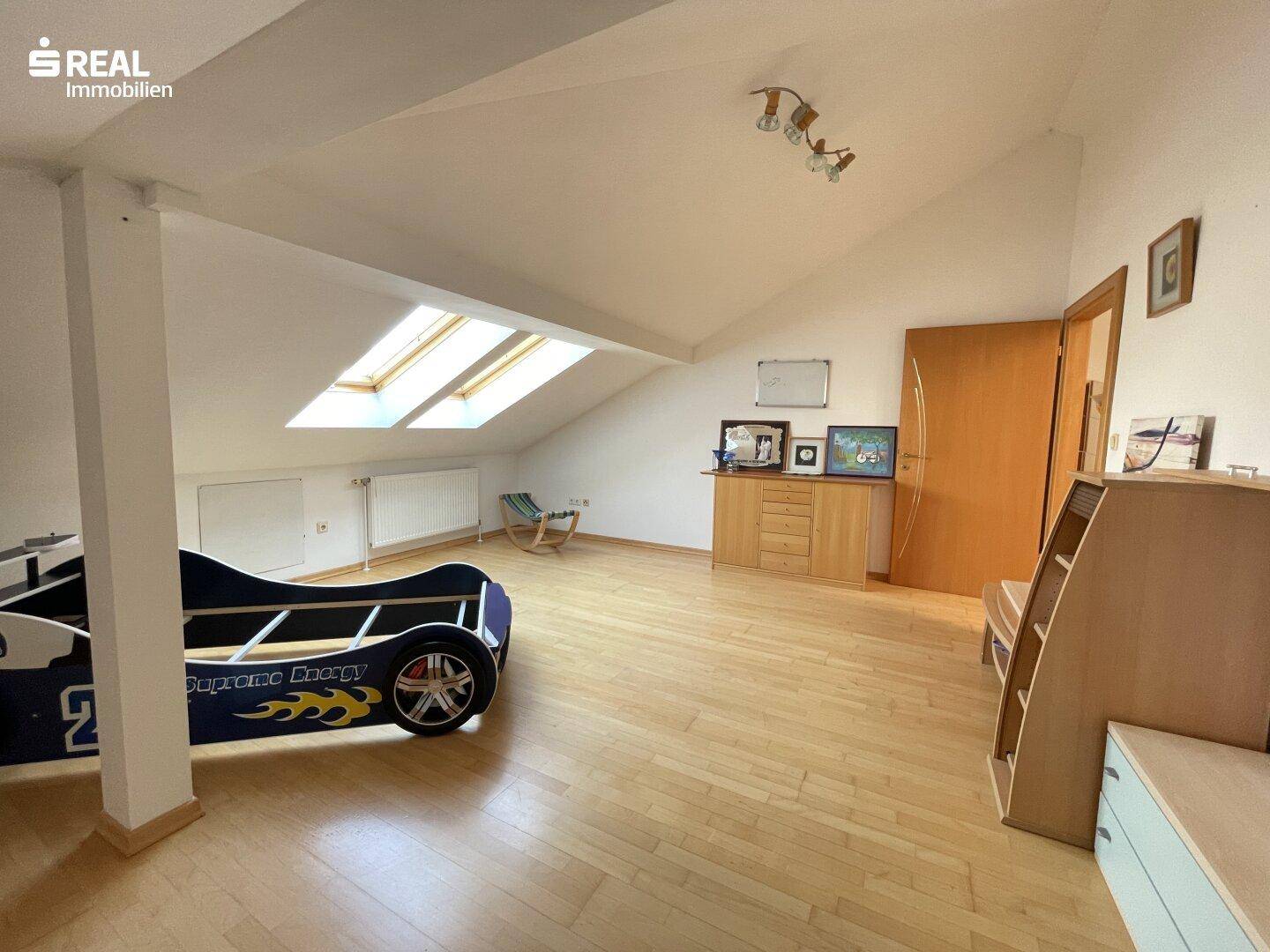Dachgeschoss-Schlafzimmer mit Holzboden, Dachfenstern und schrägen Wänden.