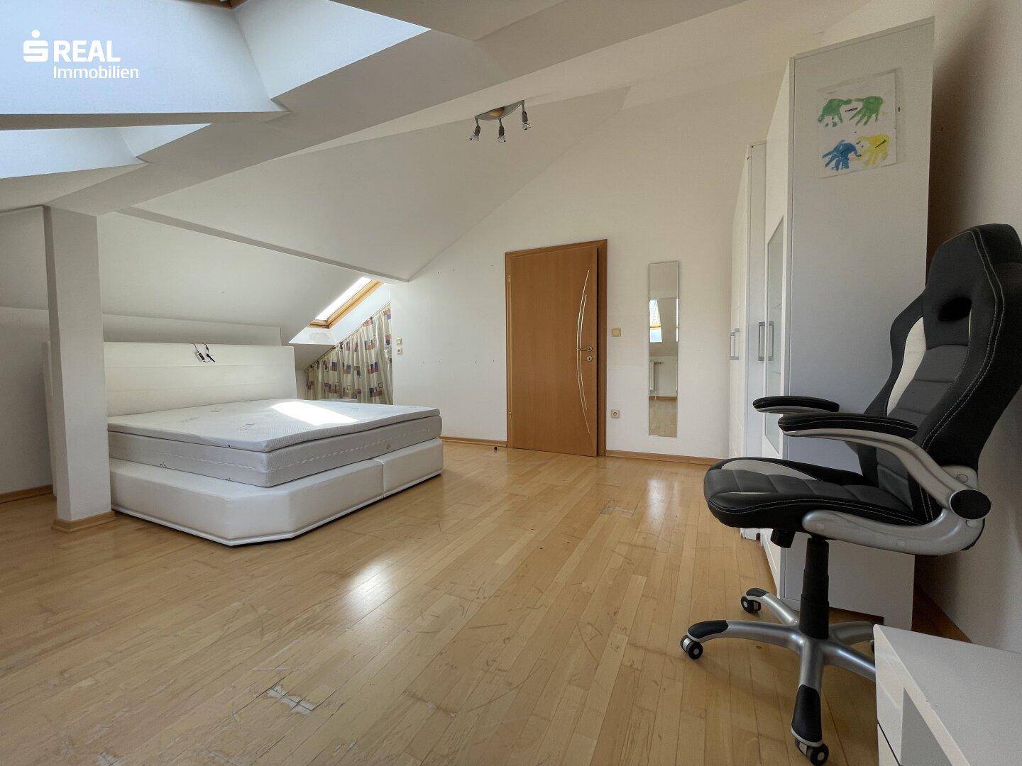Geräumiges Schlafzimmer im Dachgeschoss mit Holzboden und viel natürlichem Licht.