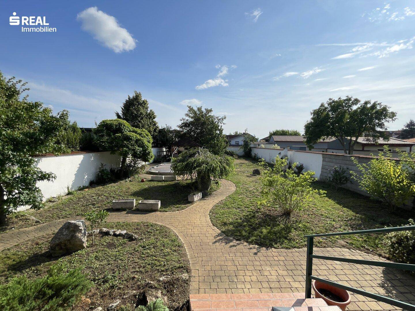 Großer, terrassierter Garten mit gepflasterten Wegen, Rasenflächen und verschiedenen Pflanzen.