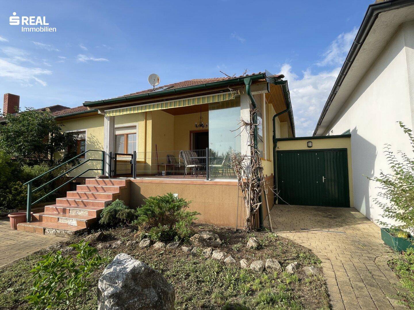 Hausansicht mit überdachter Terrasse, Außentreppe und angrenzender Garage.