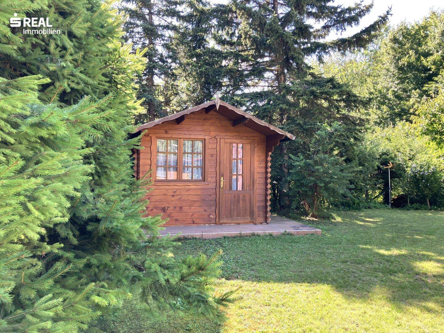 Charmantes Gartenhaus aus Holz inmitten eines grünen Gartens, umgeben von Bäumen und Natur.