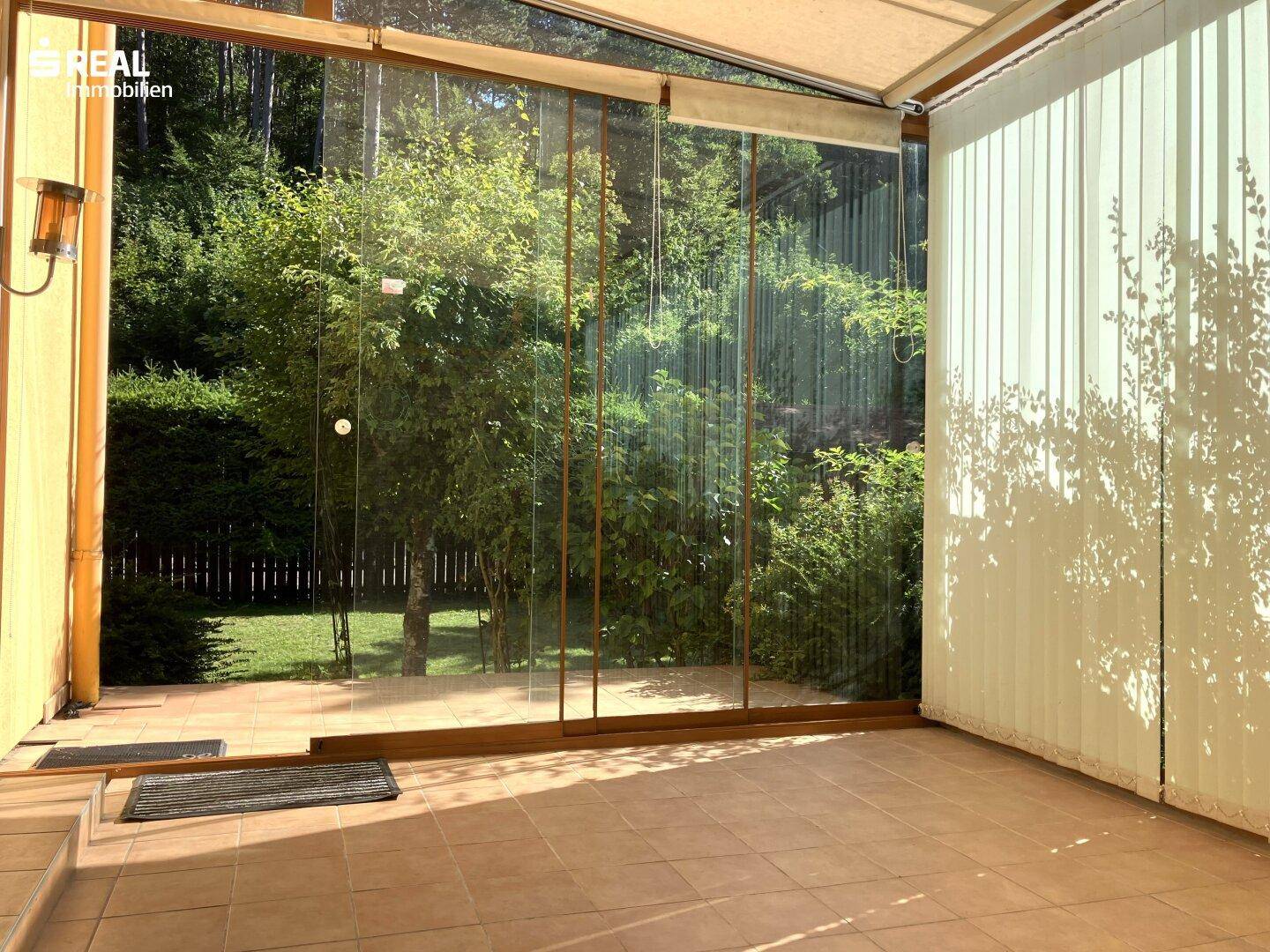 Heller Wintergarten mit großen Glasfronten und Blick ins Grüne, ideal für entspannte Stunden.