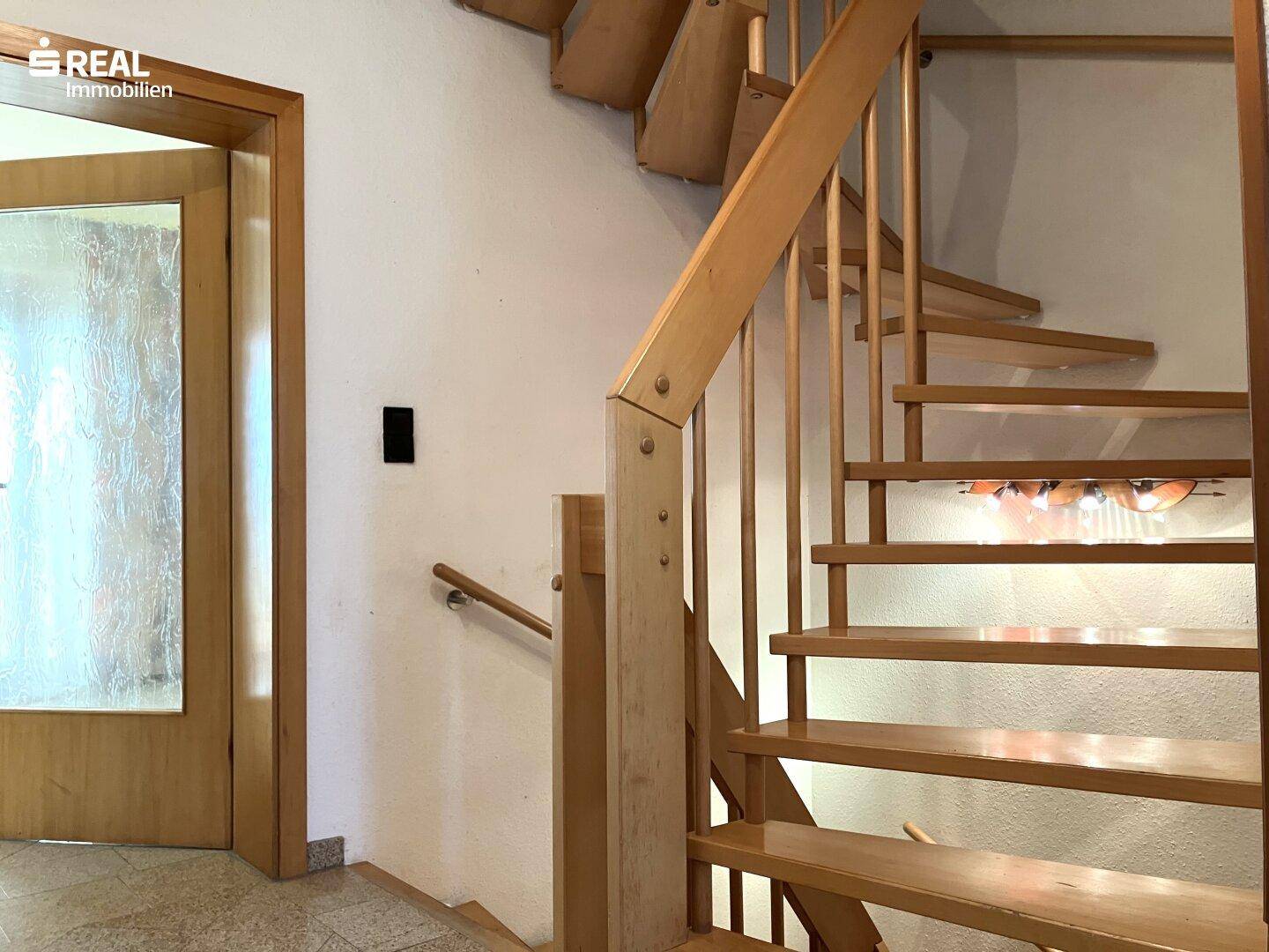 Helle Holztreppe mit offenem Design und Geländer, die zu den oberen Etagen des Hauses führt.