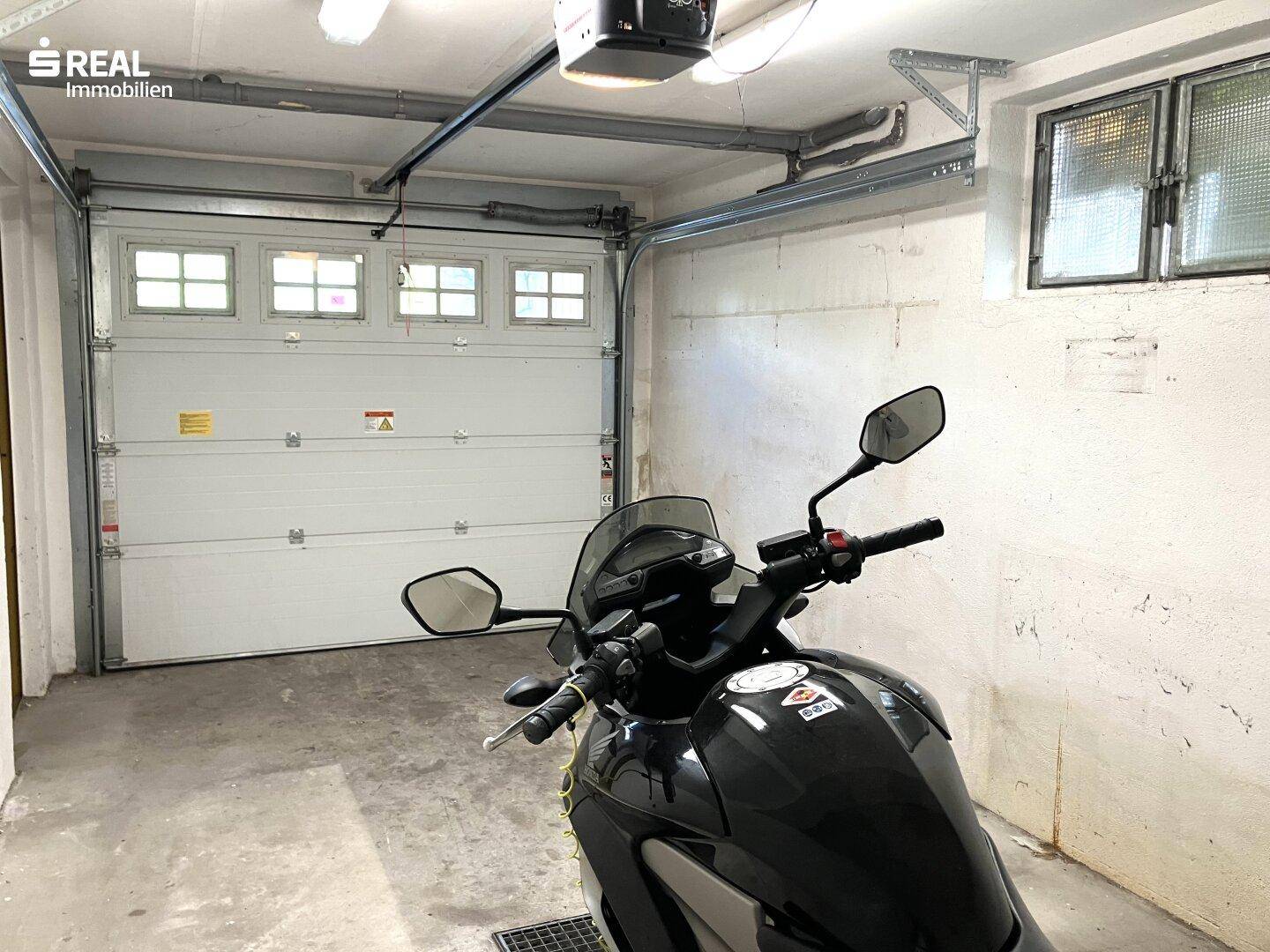 Geräumige Garage mit einem Rolltor und Fenstern, bietet Platz für Fahrzeuge und zusätzlichen Stauraum.