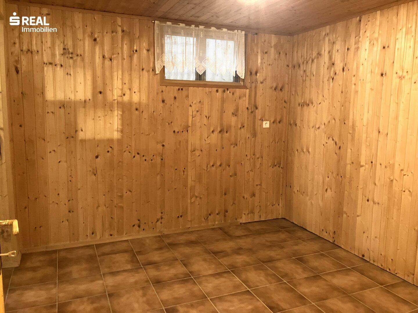 Raum mit rustikaler Holzvertäfelung an den Wänden und braunen Bodenfliesen, bietet vielseitige Nutzungsmöglichkeiten.