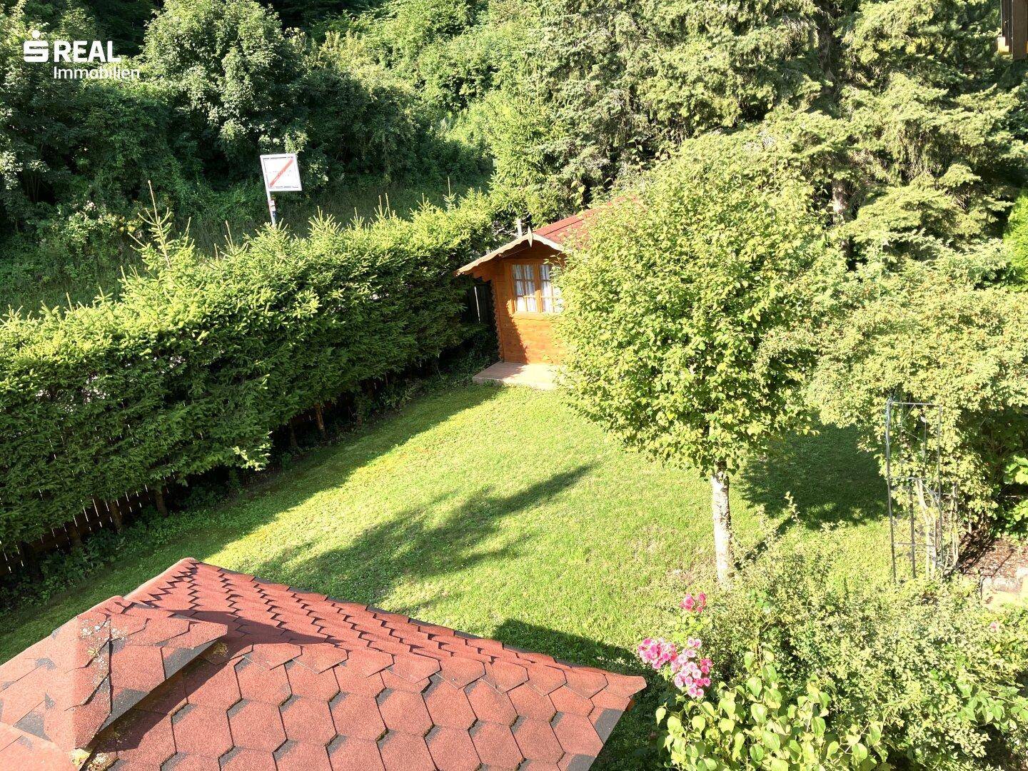 Gepflegter Gartenbereich mit Rasenfläche, hohen Hecken und einem kleinen Gartenhaus im Grünen.