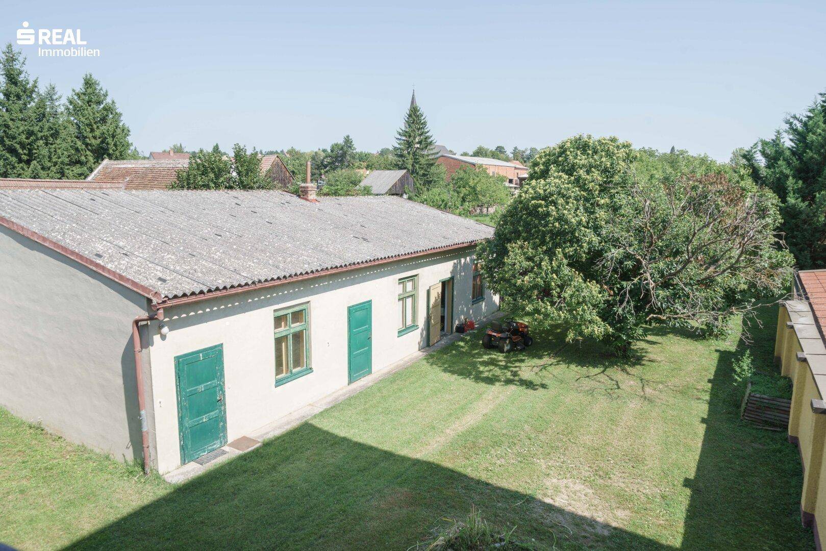 Großer Gartenbereich mit Rasenfläche und altem Baumbestand neben einem Nebengebäude.