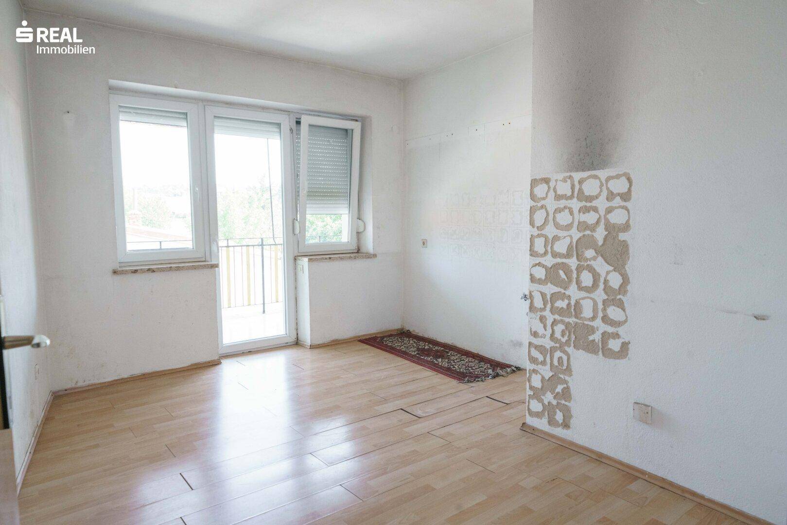 Helles Zimmer mit Laminatboden und Zugang zu einem französischen Balkon, renovierungsbedürftig.