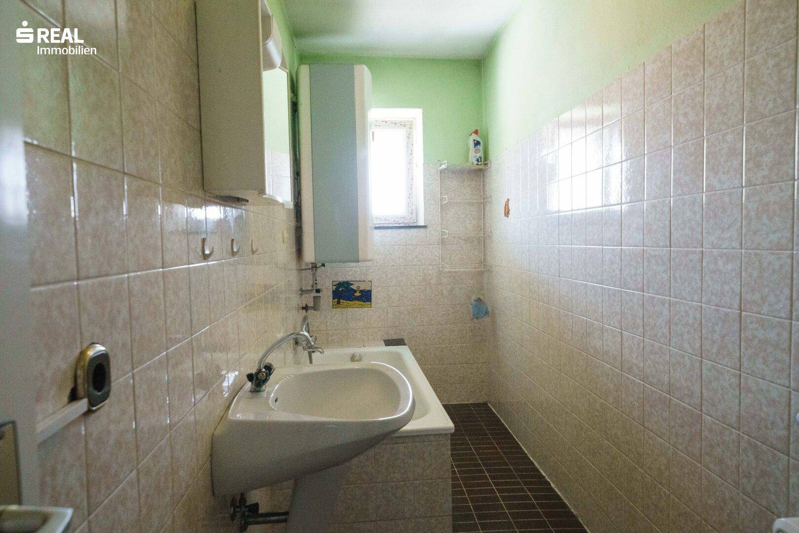 Gefliestes Badezimmer mit Waschbecken, Badewanne und kleinem Fenster, im Stil der 80er Jahre.