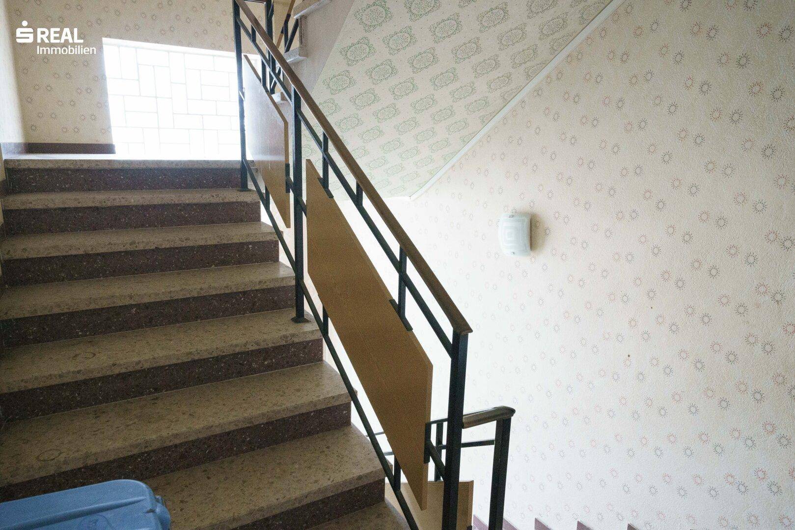 Treppenhaus mit Terrazzostufen und gemusterter Tapete, führt in die oberen Stockwerke.