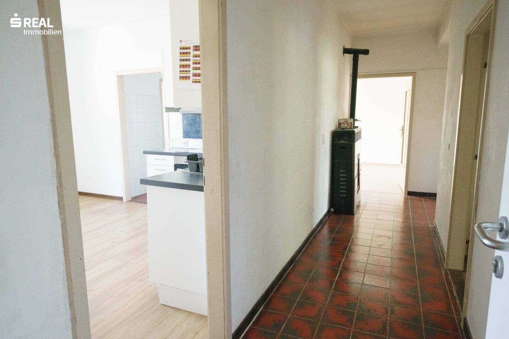 Flur mit Fliesenboden und einem Holzofen, der zu einer offenen Küche führt.