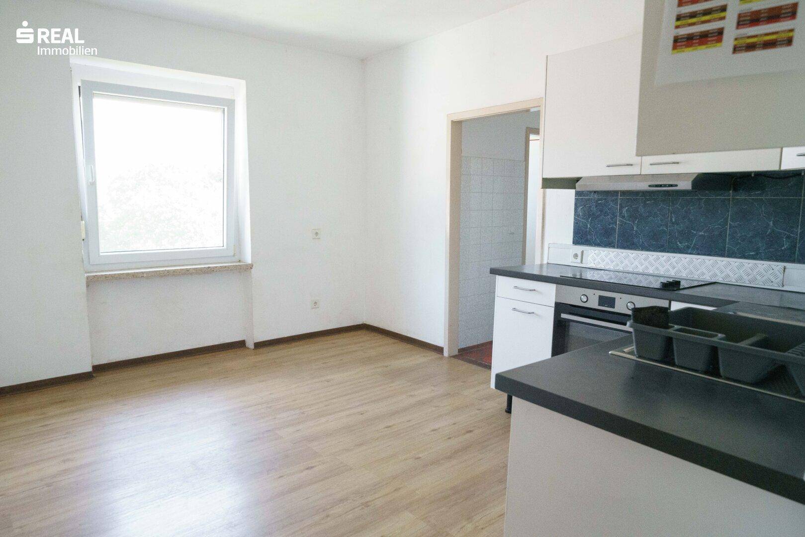 Küche mit Laminatboden, Fenster und Einbauküche mit Herd und Dunstabzugshaube.