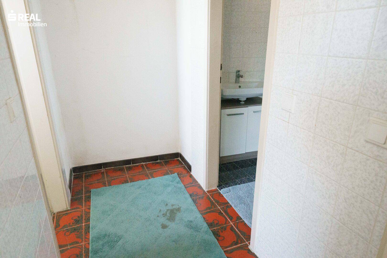 Kleiner Eingangsbereich zu einem Badezimmer mit Fliesenboden und Waschbecken im Hintergrund.