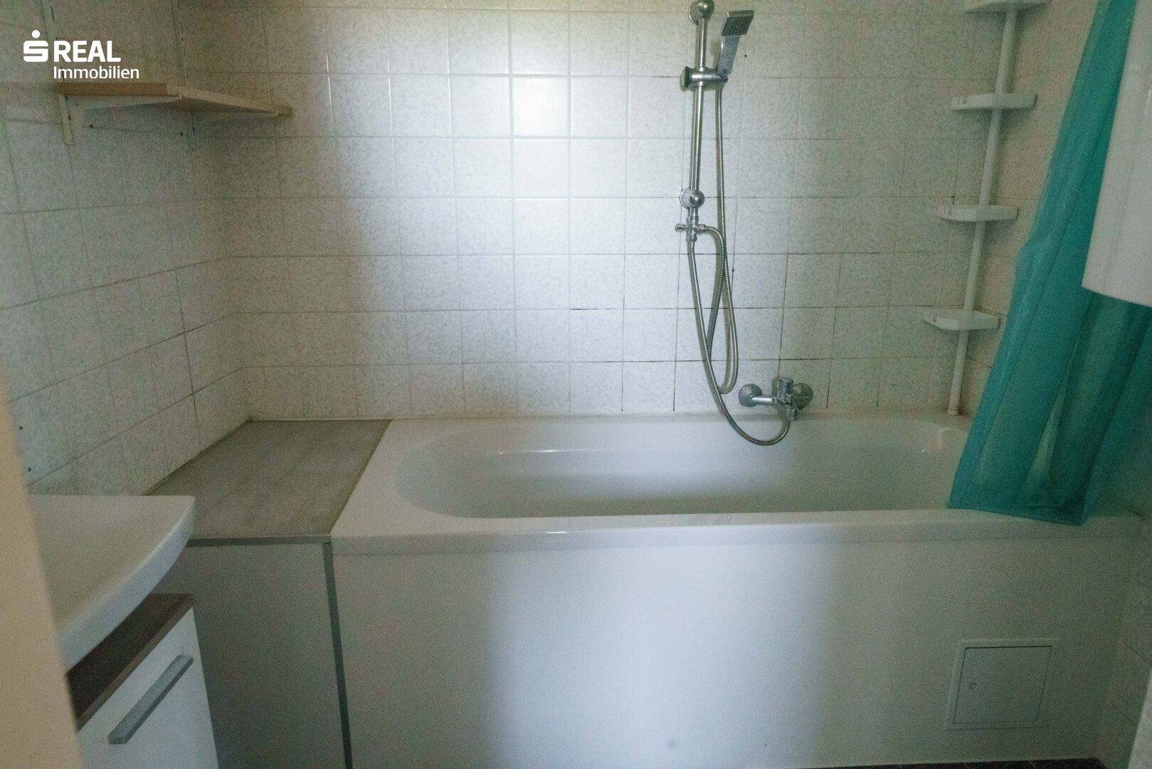 Badezimmer mit Badewanne und Duschvorrichtung, komplett gefliest in hellem Design.