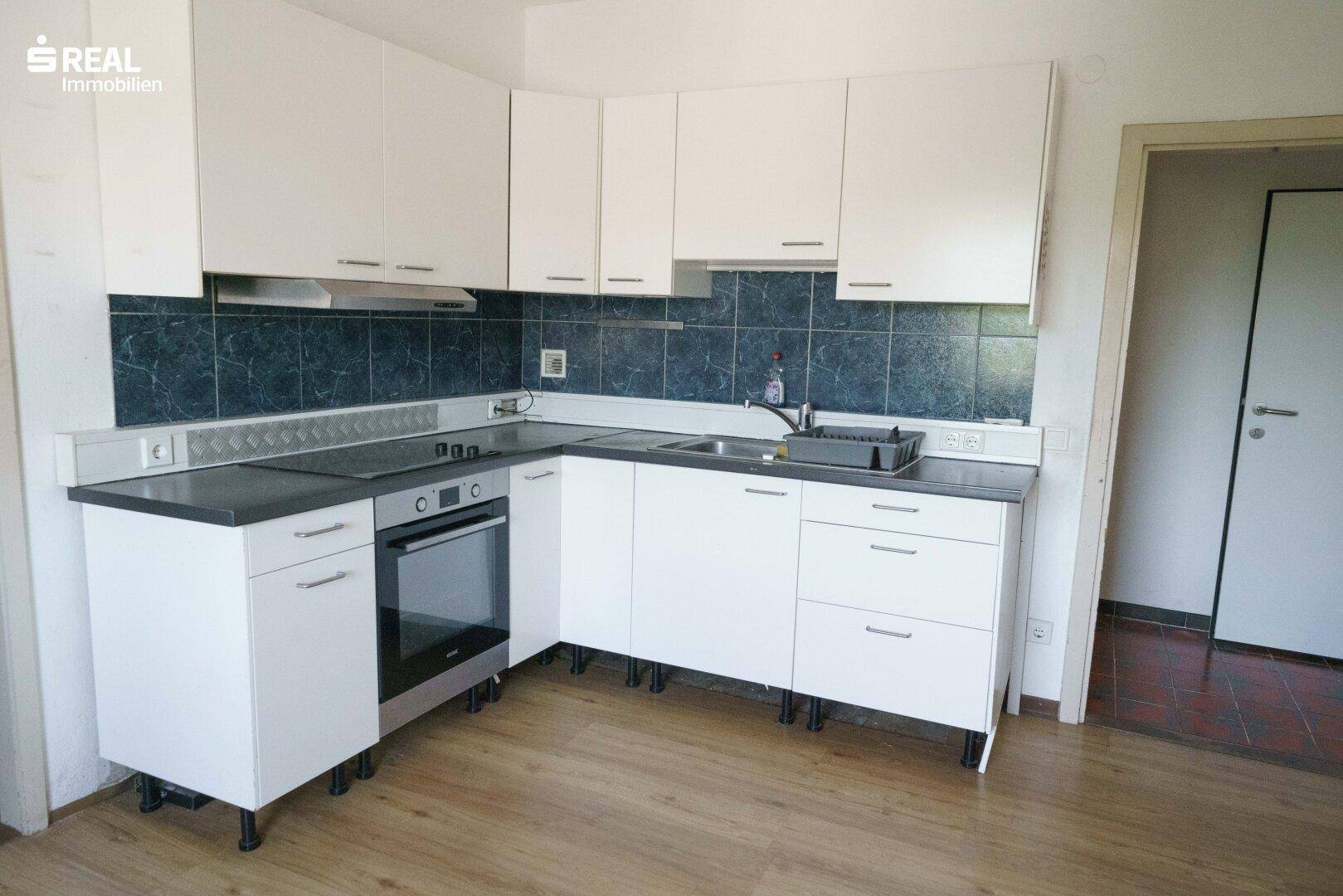 Funktionale Einbauküche mit weißen Schränken, Herd und Dunstabzugshaube, renovierungsbedürftig.