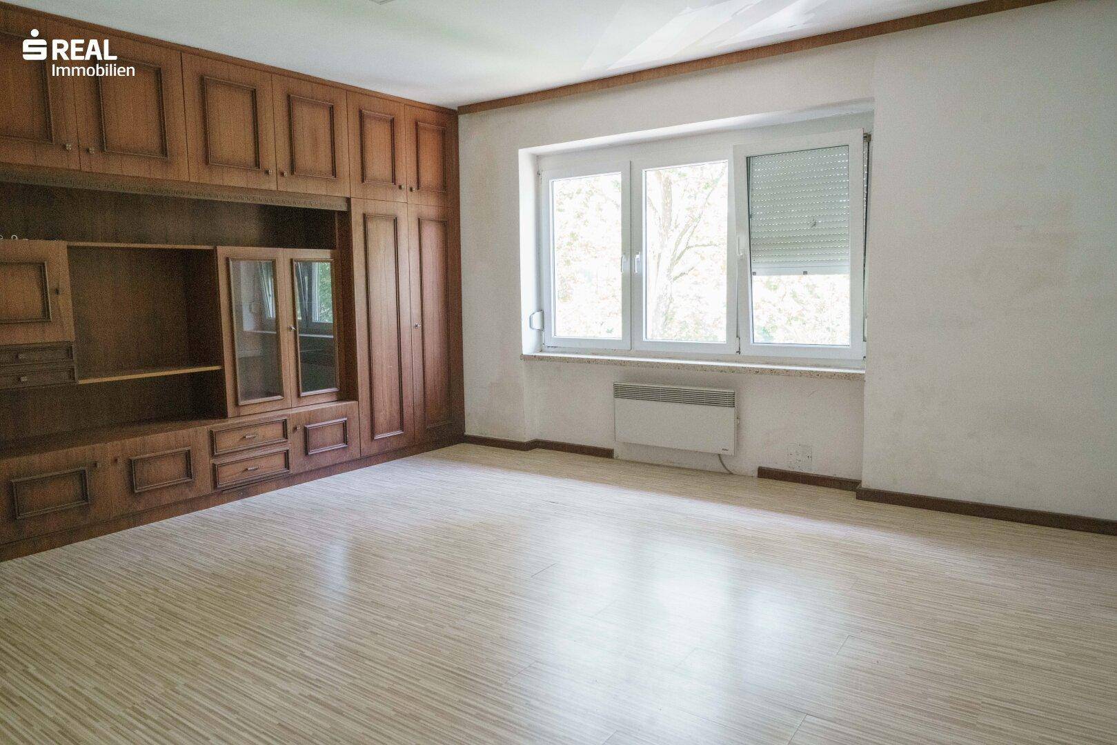 Helles Zimmer mit Laminatboden und großer Fensterfront, ausgestattet mit Holzmöbeln.