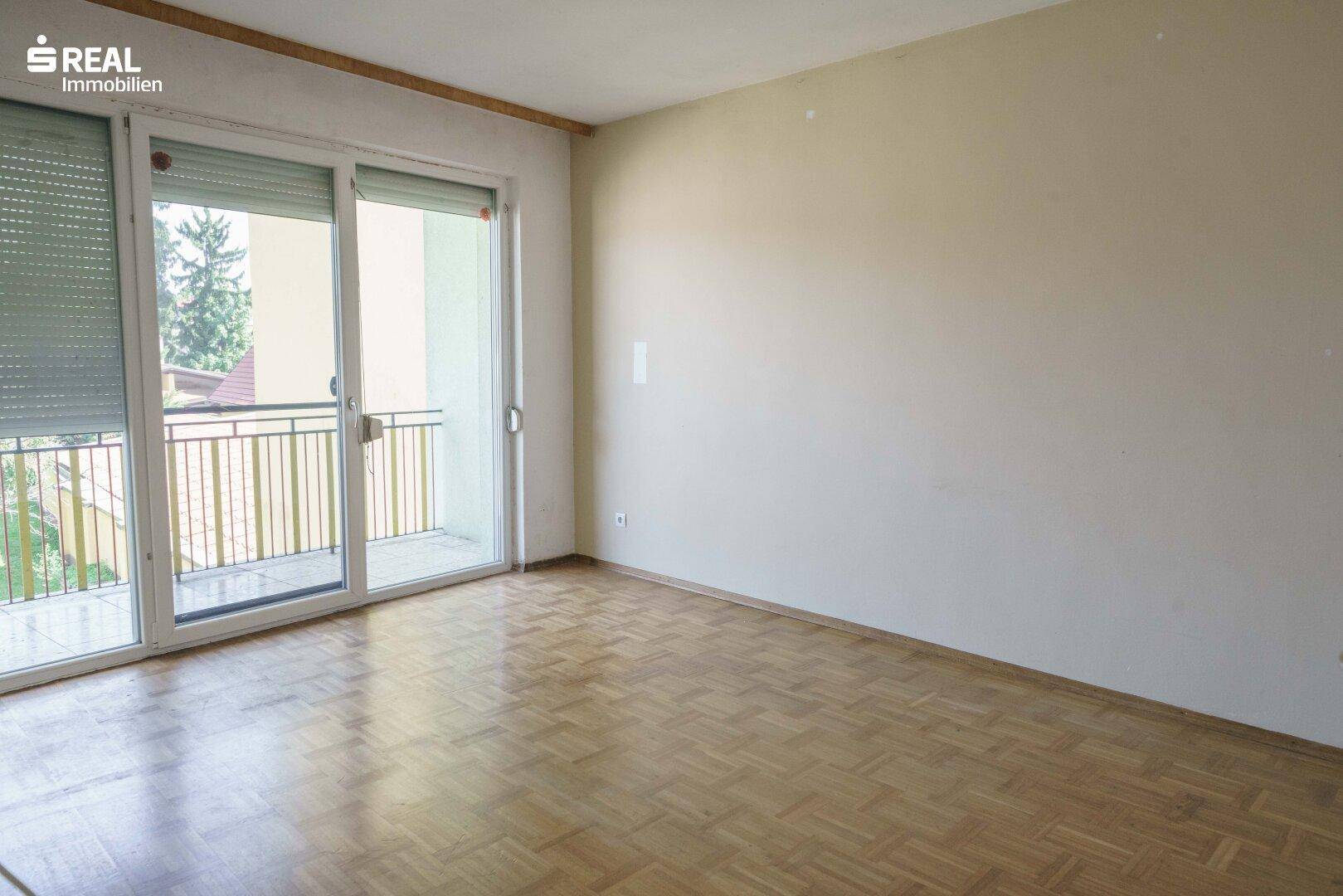 Zimmer mit Laminatboden und breiter Balkontür, die viel Licht hereinlässt.