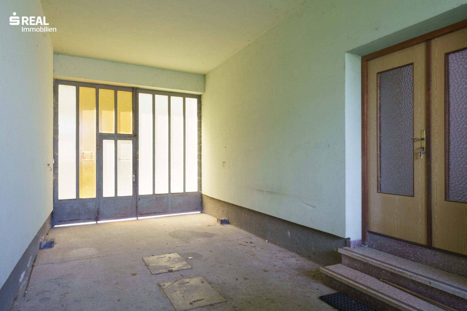 Überdachter Eingangsbereich mit Garagentor und separater Haustür, bietet Schutz.