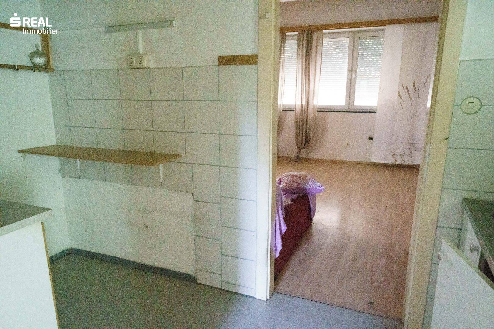 Kleiner Küchenbereich mit Fliesenwand, führt zu einem angrenzenden Zimmer.
