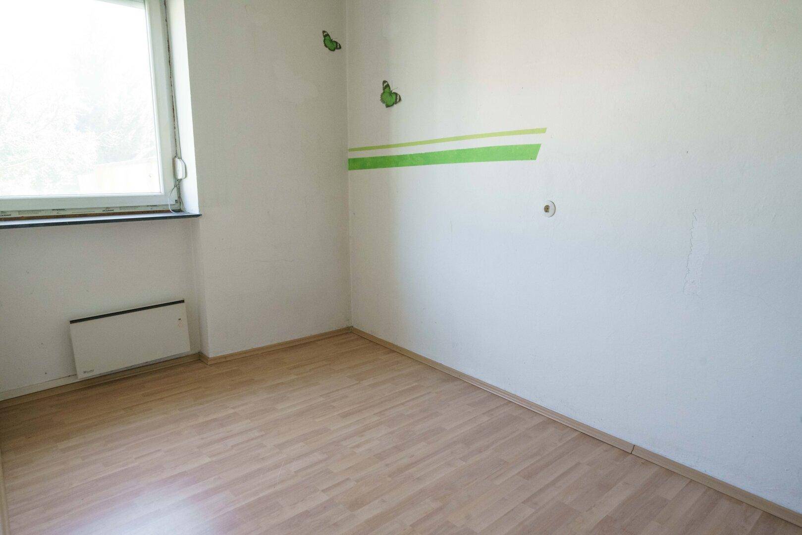 Einfaches Zimmer mit Laminatboden und einem Fenster, dekoriert mit grünen Streifen.